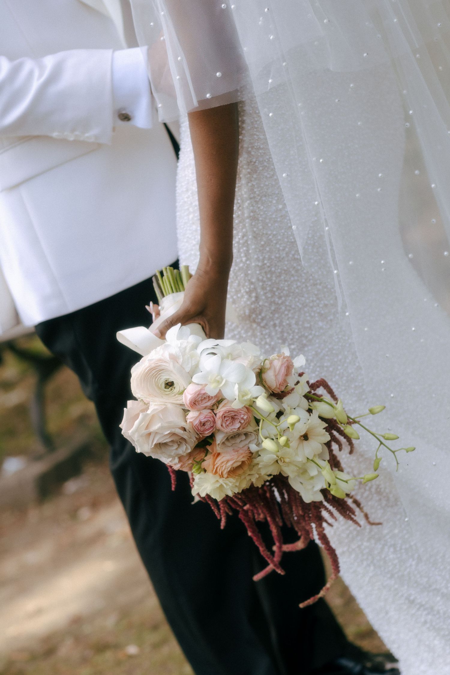 Close-up of bride and groom holding elegant pink and white wedding bouquet together.