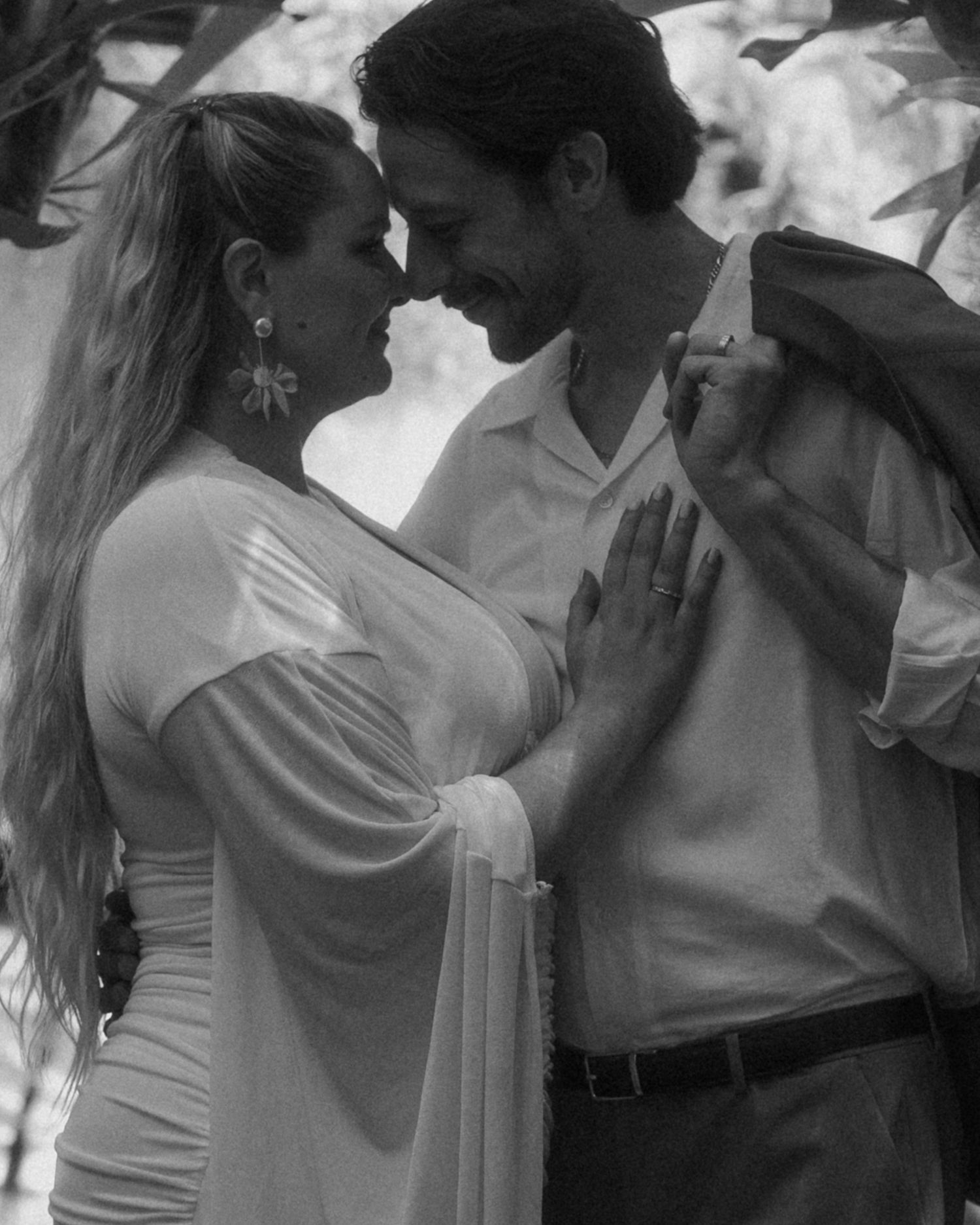 Black and white photo of a couple in romantic embrace, woman in white dress with floral earrings, man in white shirt.