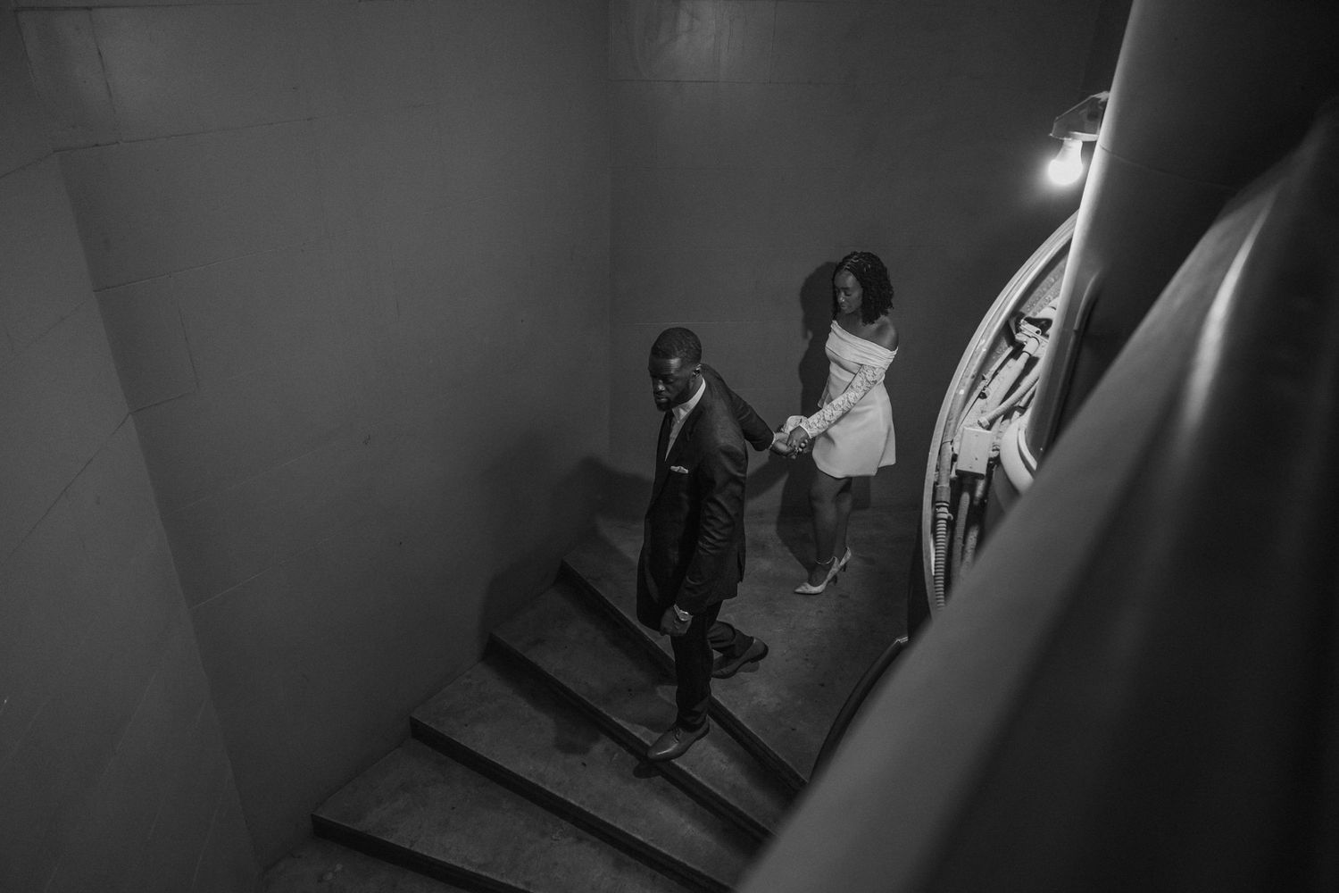 Couple holding hands walking down stairs in black and white wedding photo.