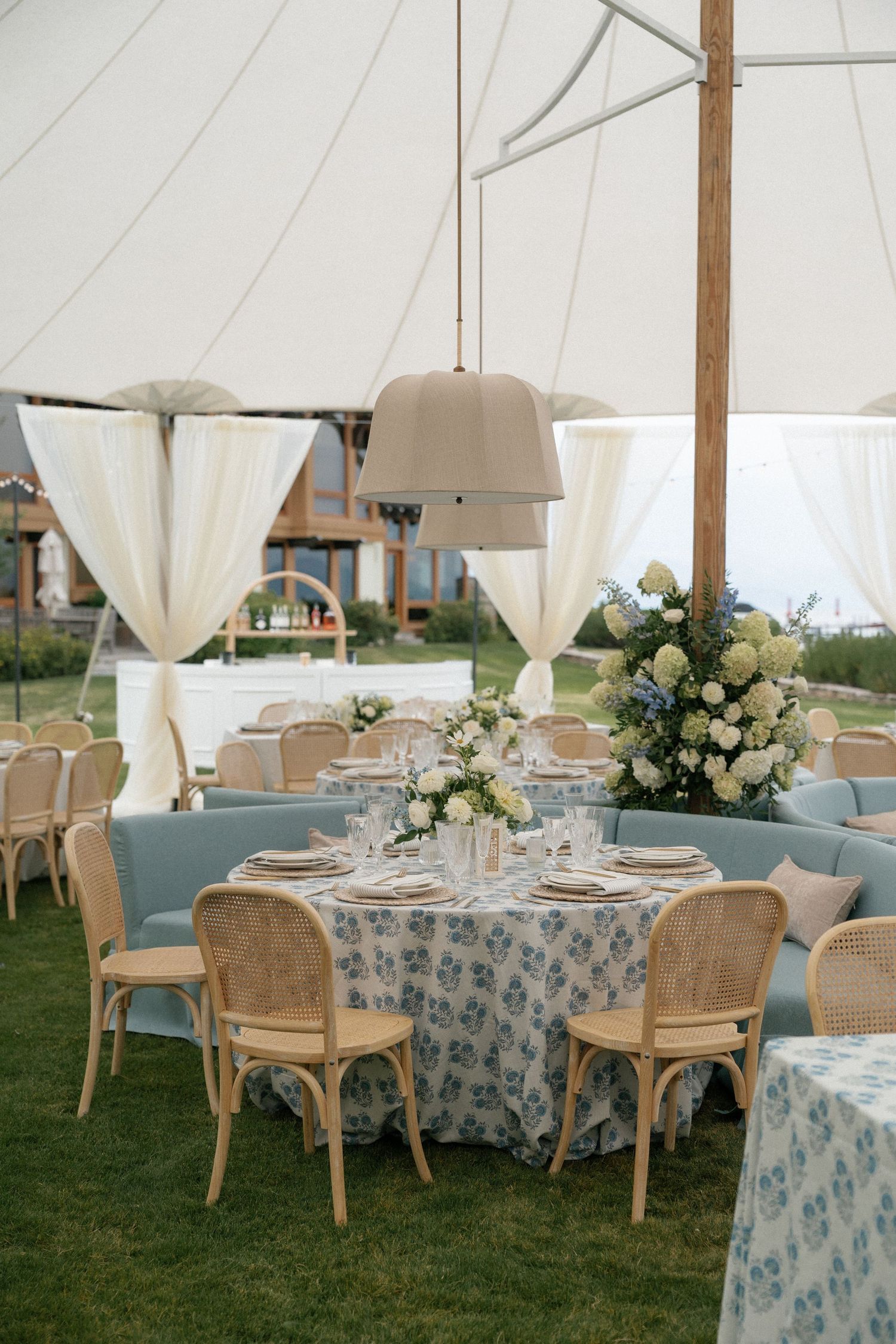 Wedding reception tables decorated with white floral centerpieces under an airy tent canopy.