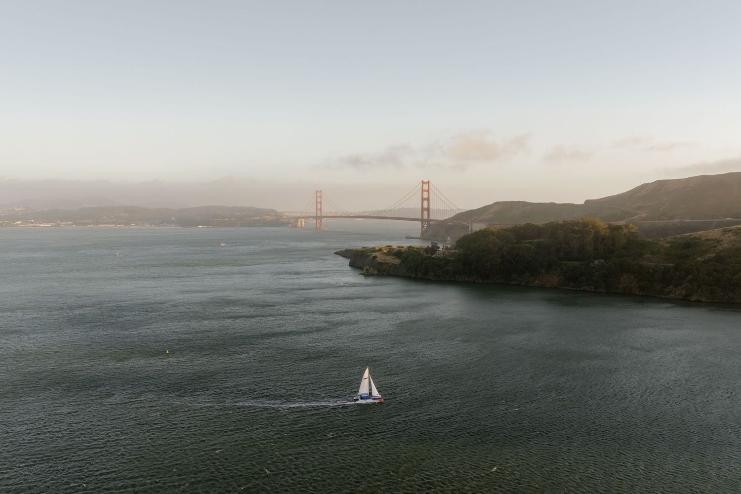 Scenic view of San Francisco Bay with Golden Gate Bridge and sailboat at sunset.