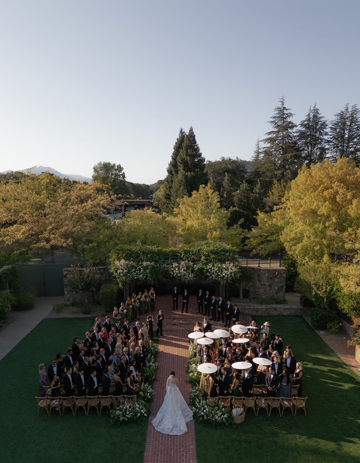 Aerial view of an outdoor wedding ceremony with guests seated in a garden setting.