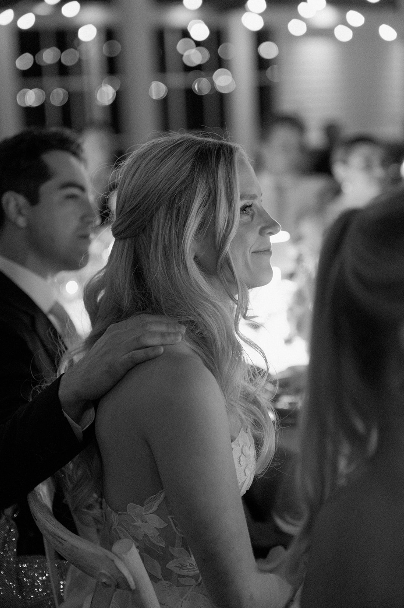 Black and white candid reception photo with bokeh lights in the background.