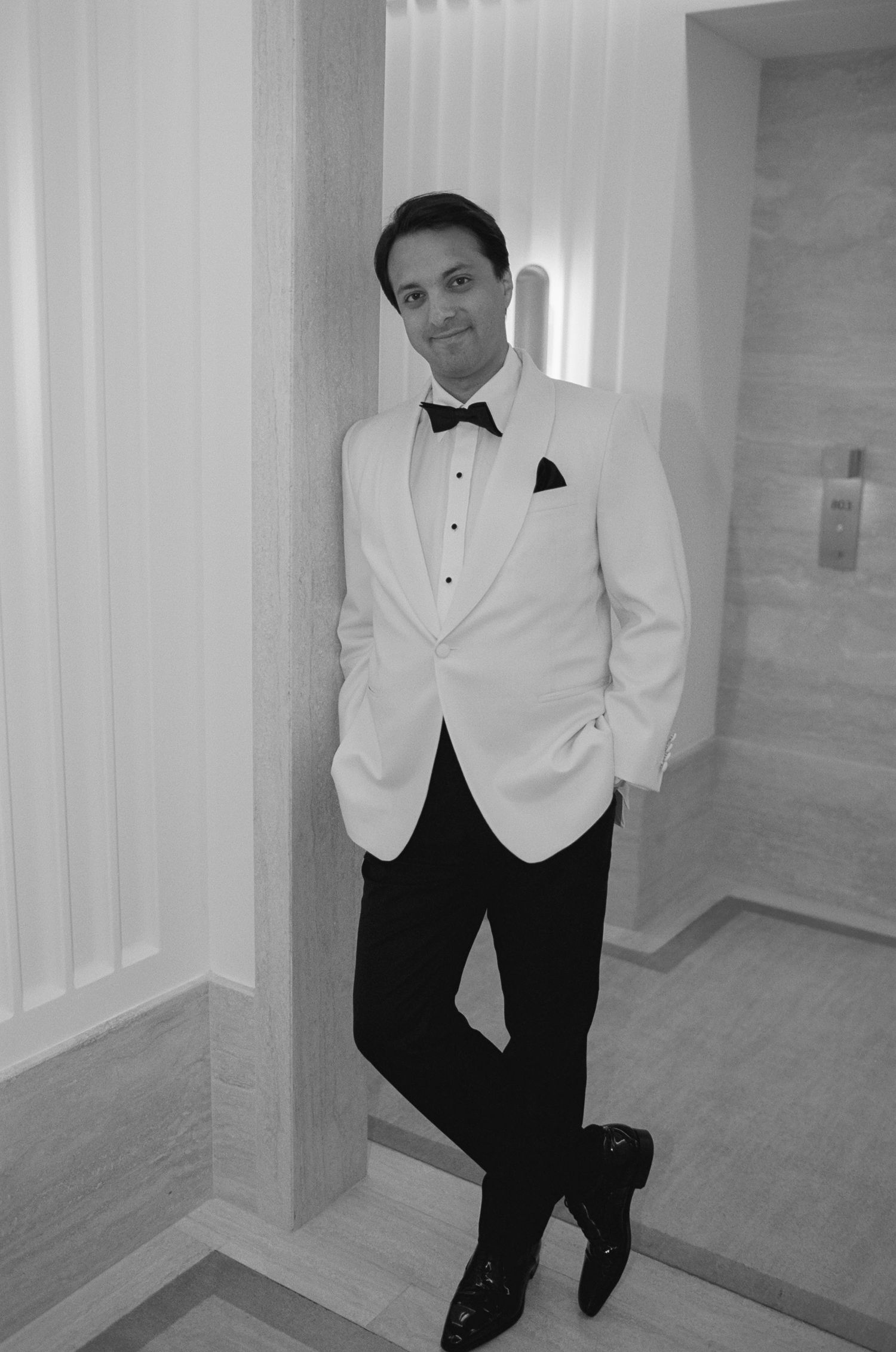 Person posing in formal black and white attire in a modern hallway.