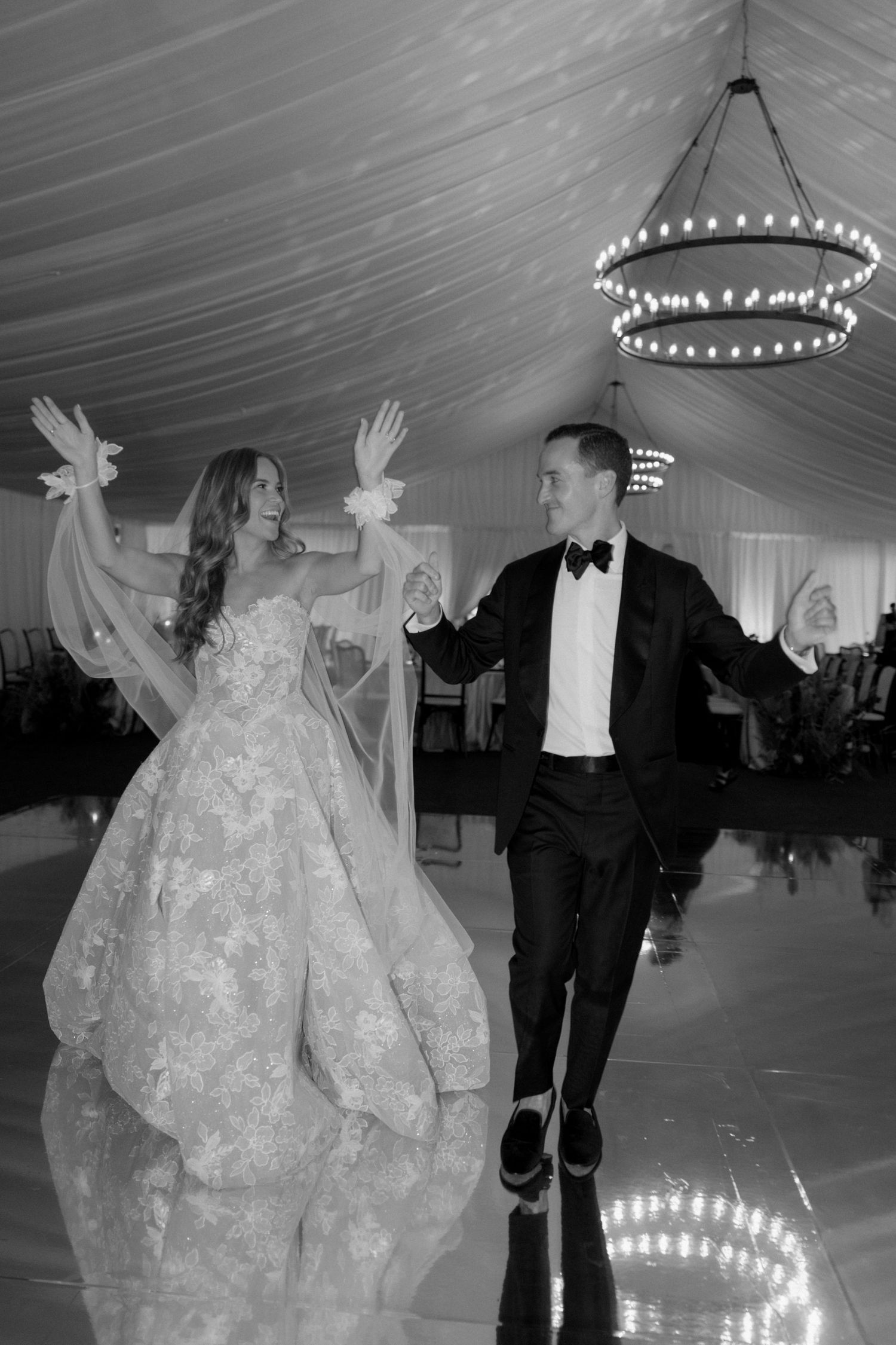 Black and white photo of dancing under twinkling lights at an elegant tented reception.