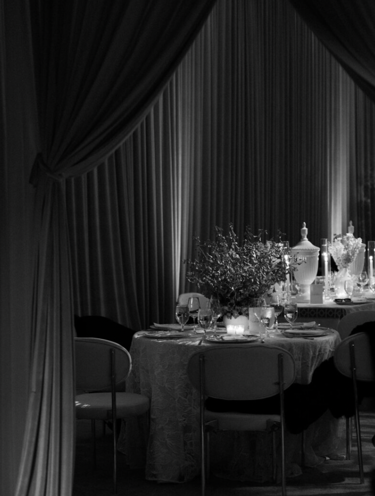 An elegant black and white photograph of a formal dining table setting with curtains, glassware and candlelight at a luxury wedding in LA.