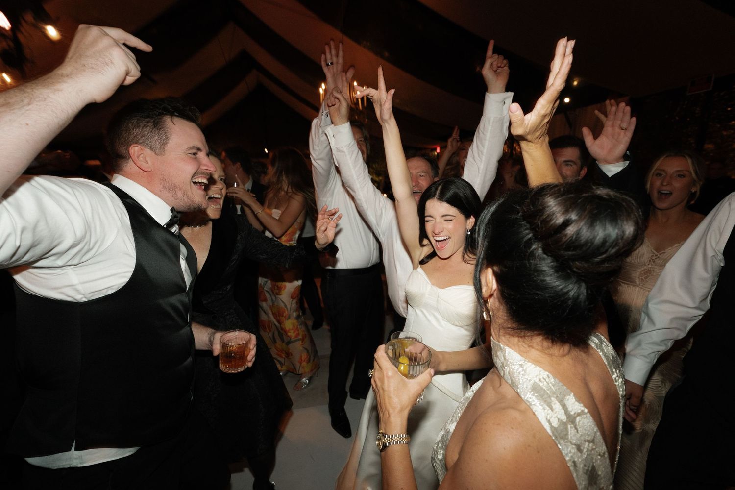 Wedding guests dance and celebrate on a dimly lit dance floor during the reception.
