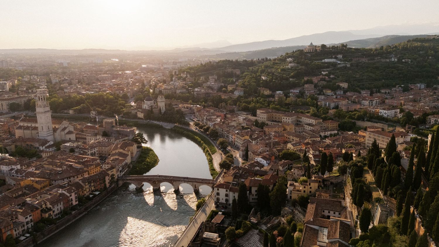 Aerial view of Verona, Italy, with the Adige River, ancient bridge, and terracotta rooftops glowing in golden sunset light.