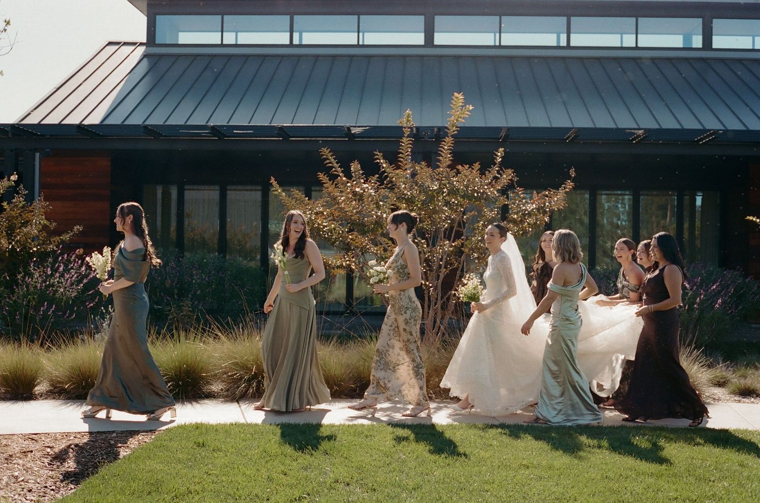 Wedding party members pose together outdoors against a modern building backdrop.