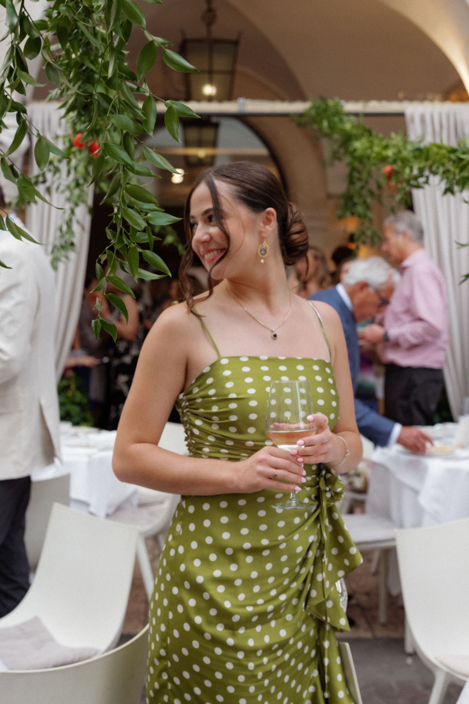 Young woman in green polka dot dress holding champagne glass at elegant outdoor wedding reception.