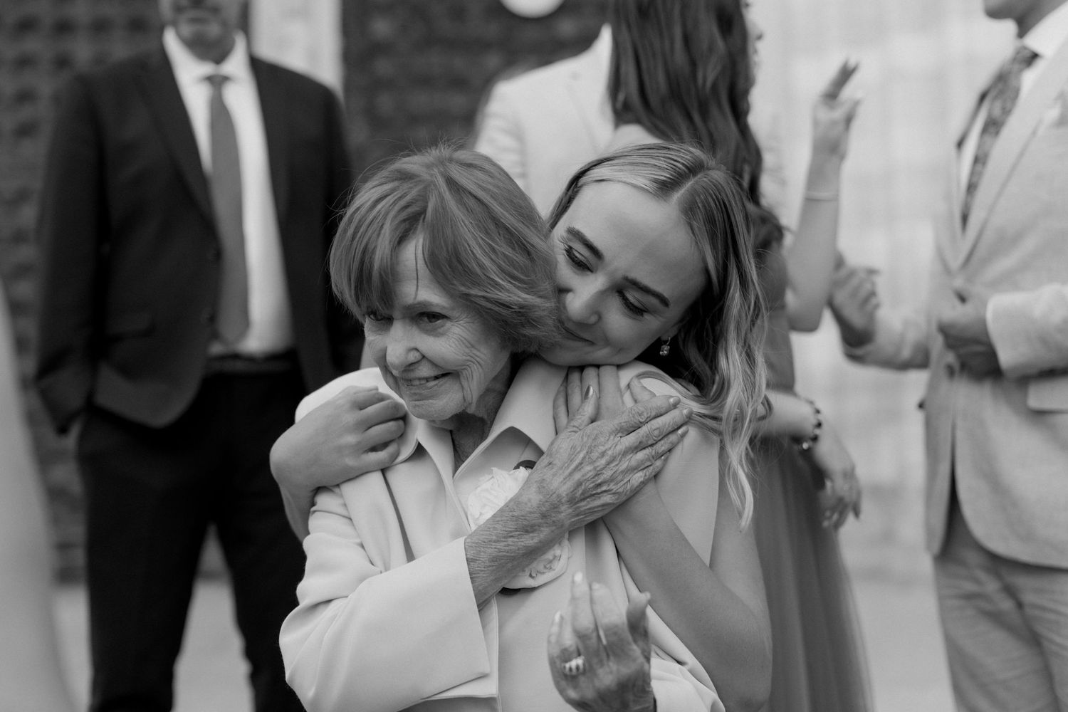 Two women share a warm hug at an outdoor event in this black and white candid photo.