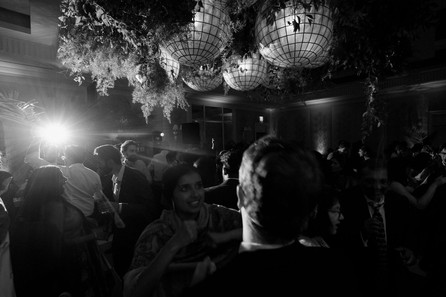Black and white photo of guests dancing at an elegant party with disco balls and greenery hanging overhead.