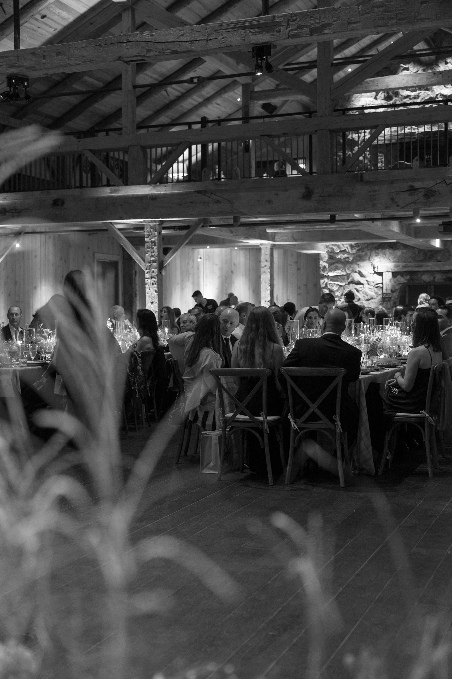 Wedding reception venue with exposed beams and dancing guests in a dimly lit rustic barn.