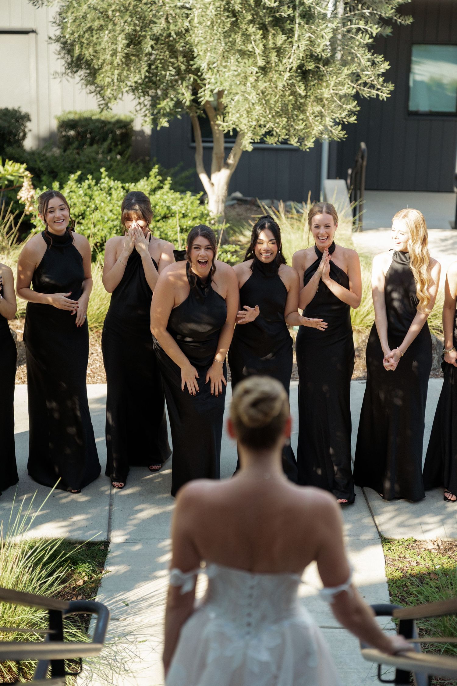 Bridesmaids in matching black dresses pose outdoors with the bride in white.
