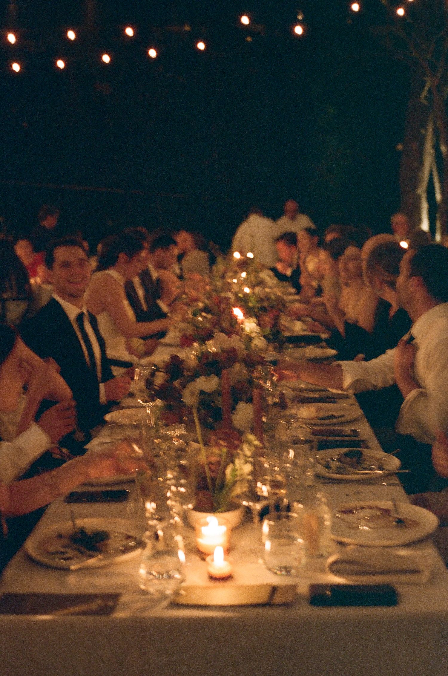 Candlelit wedding reception dinner table with string lights overhead and elegant table settings.