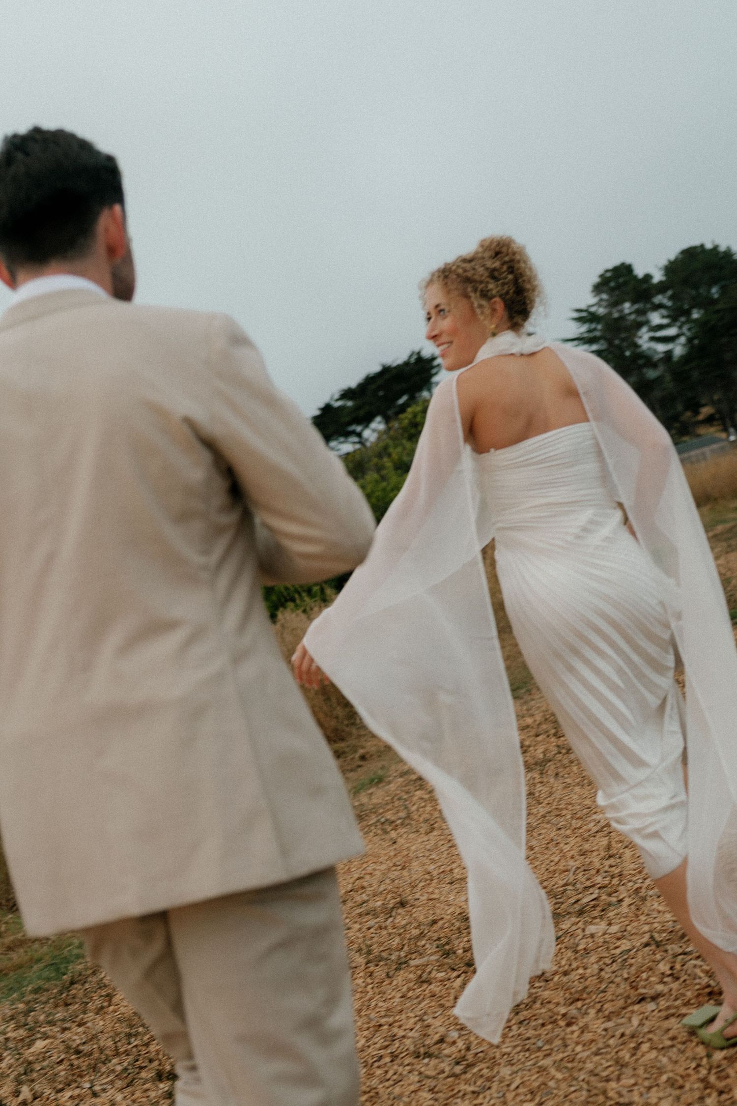 Couple in white and beige formal attire walking along a coastal path.