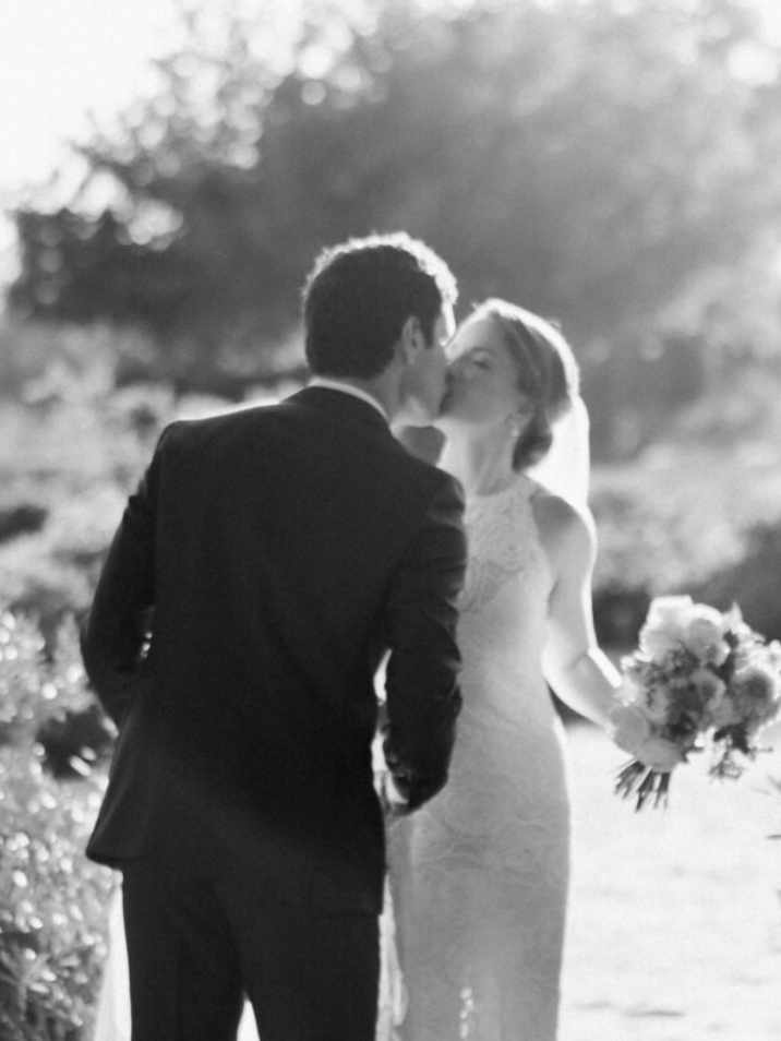 A couple walks hand in hand through a sunlit garden on their wedding day.