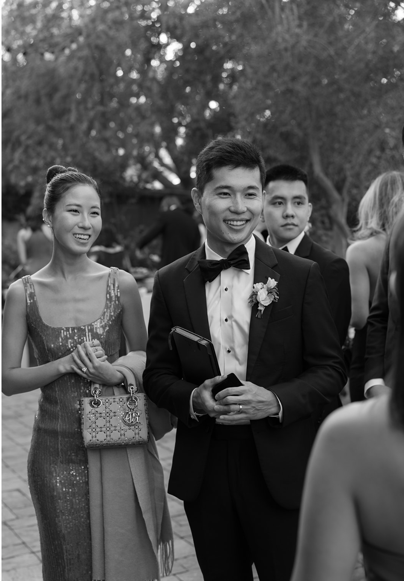 Wedding guests in formal attire gathered outdoors for celebration photos.