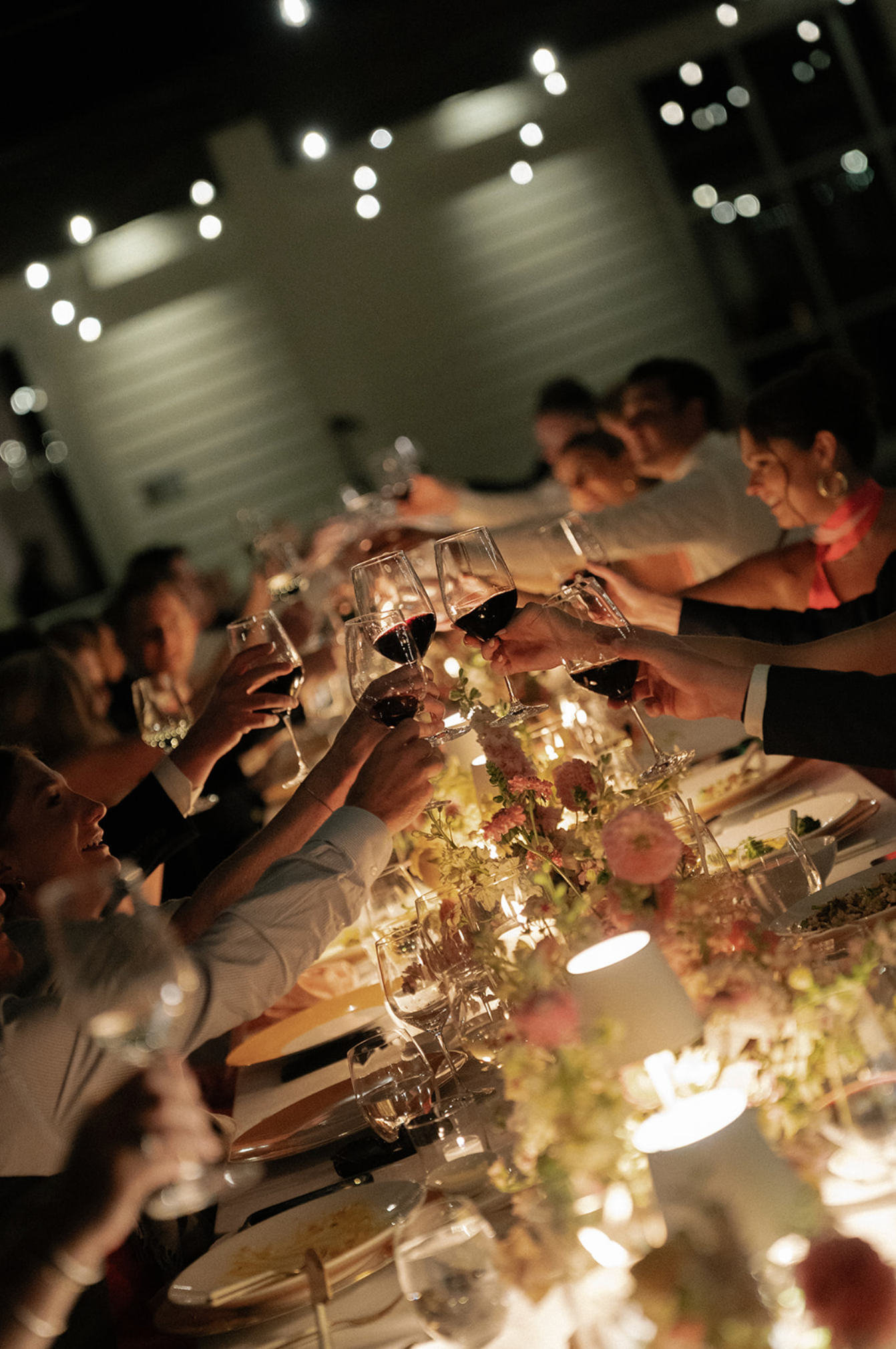 Wedding guests raising glasses for a toast at an elegantly lit dinner table.