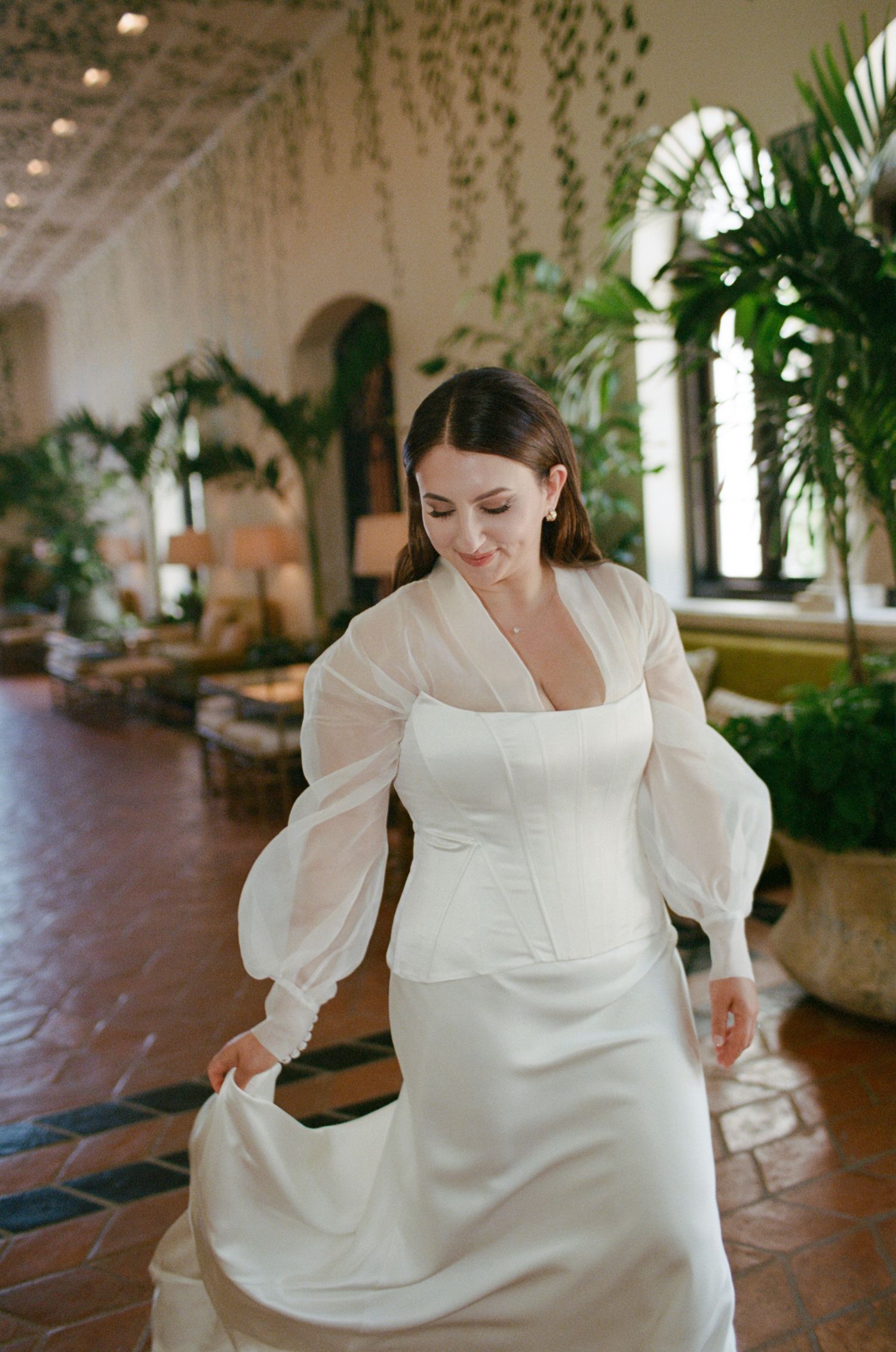 Bride in flowing white dress with billowing sleeves twirling on terracotta tiles.