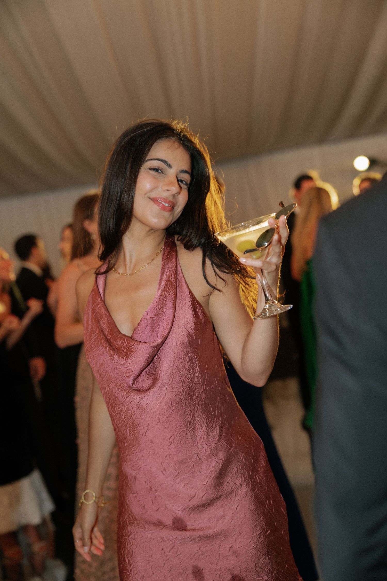 Wedding guest in a rose-colored dress dancing at an indoor reception.