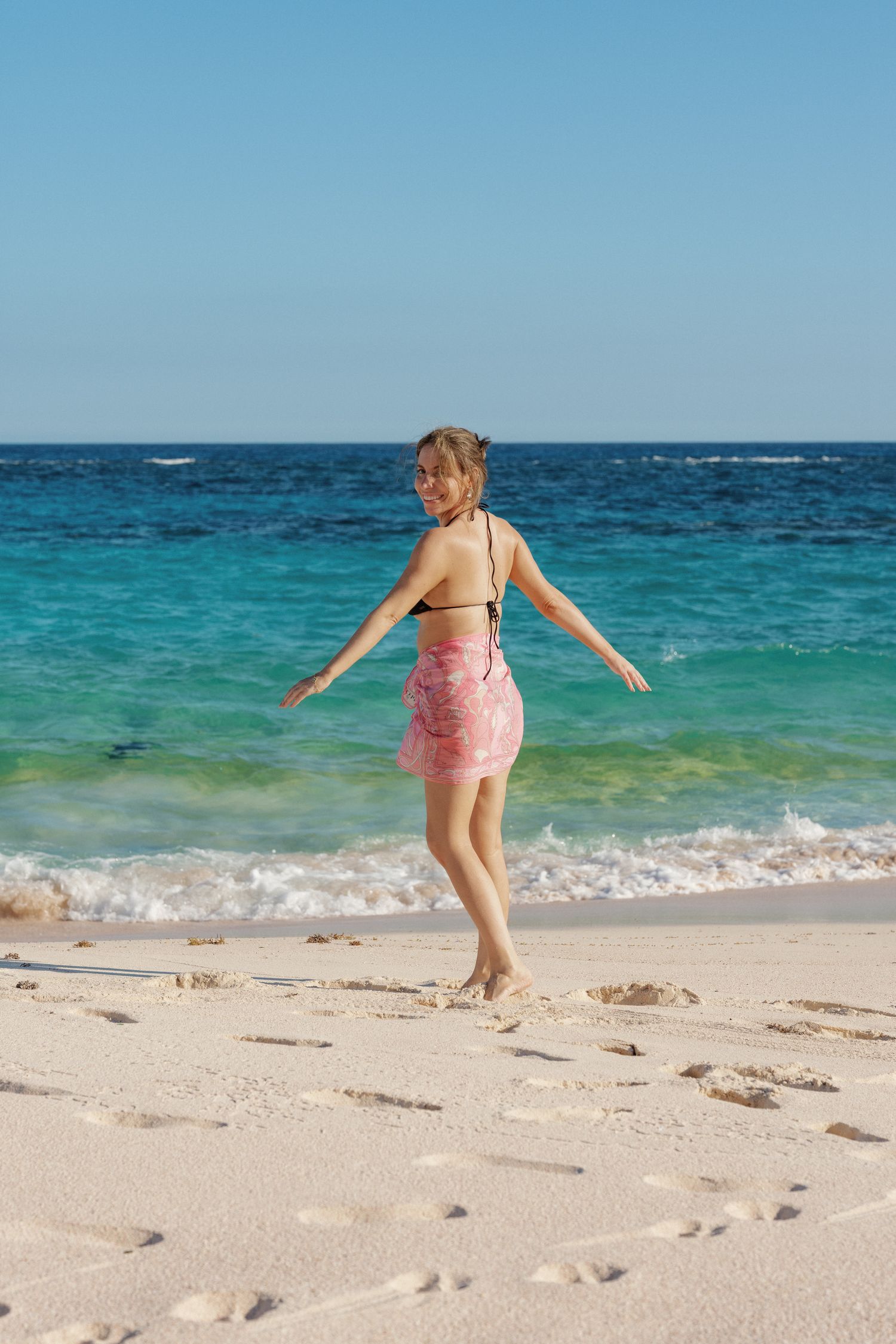 A young girl in a pink swimsuit runs along the beach with the ocean in the background.