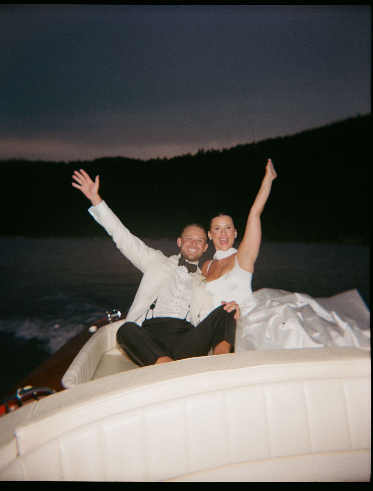 Joyful couple with raised arms posing on a boat during sunset.