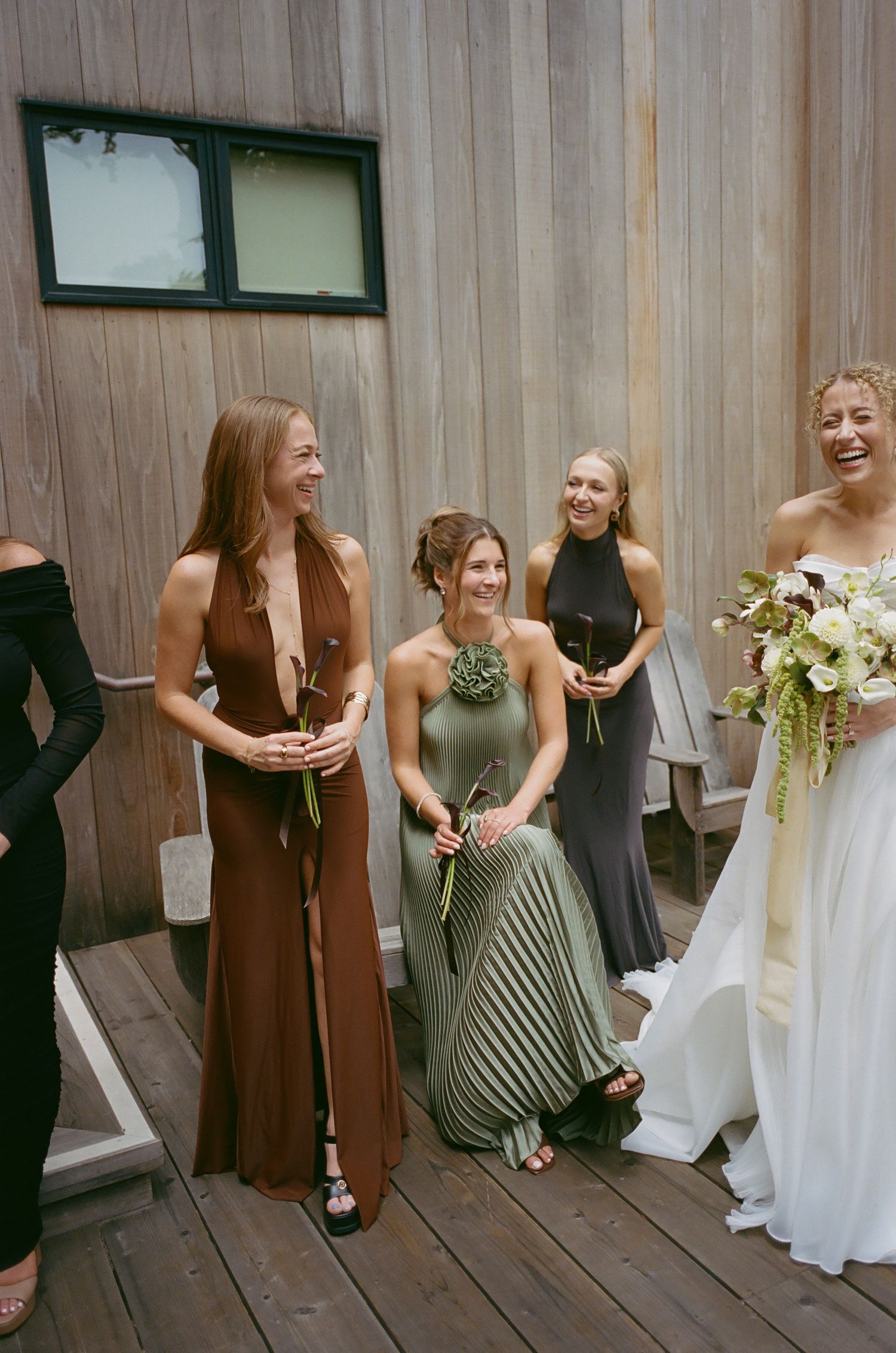Wedding party in brown and white dresses laughing together on a wooden deck.
