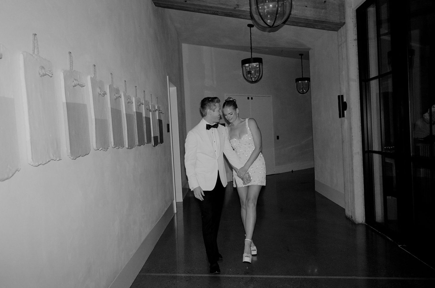 A couple in formal attire walking down a hallway in black and white.