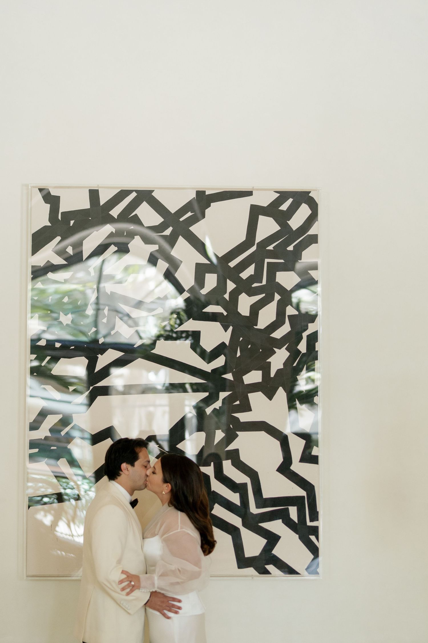 A romantic moment captured against modern artwork featuring bold black geometric patterns on a white wall.