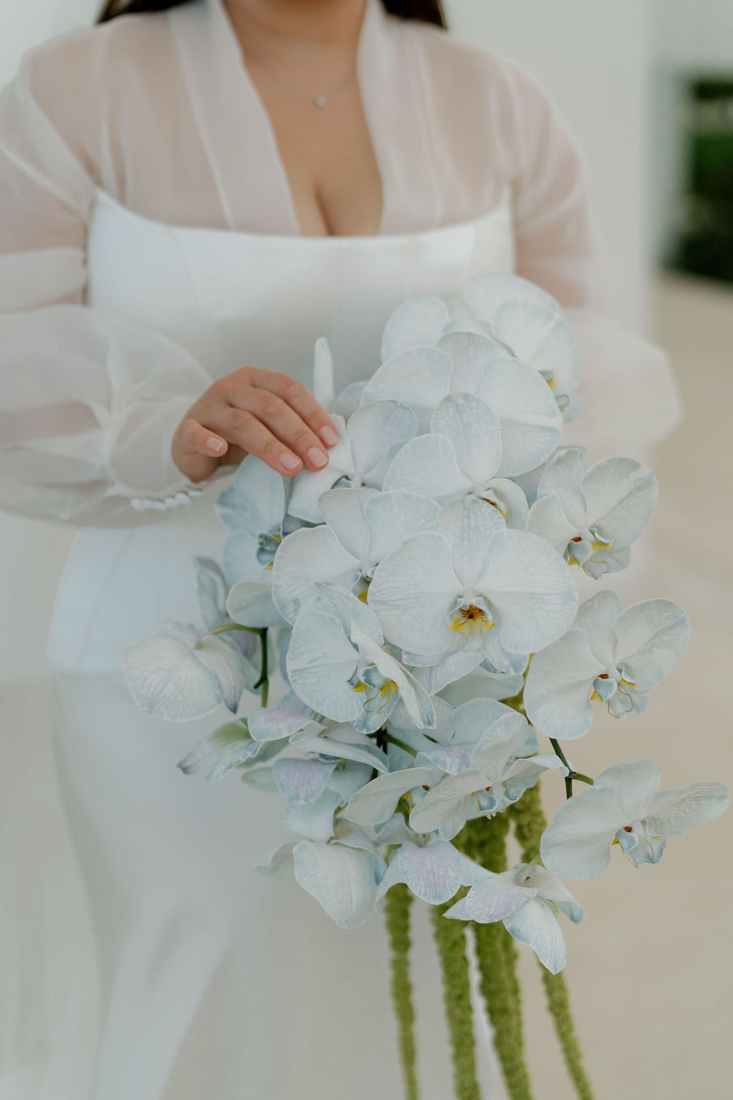 Elegant white orchid and amaranthus wedding bouquet held by bride in white dress.
