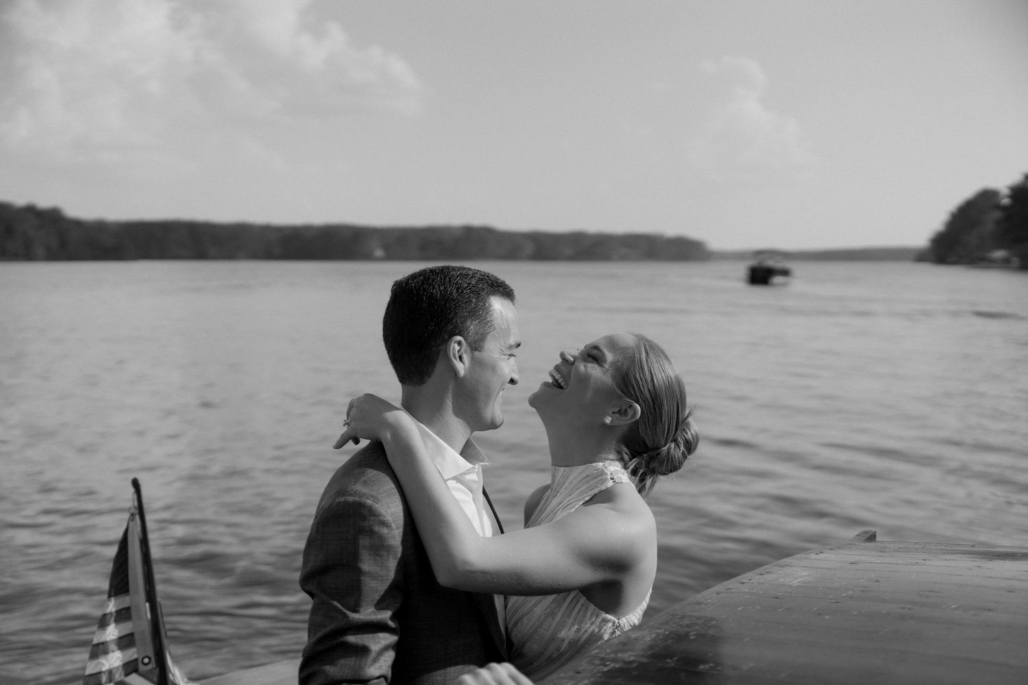 A romantic couple embraces while standing in a lake with trees in the background.