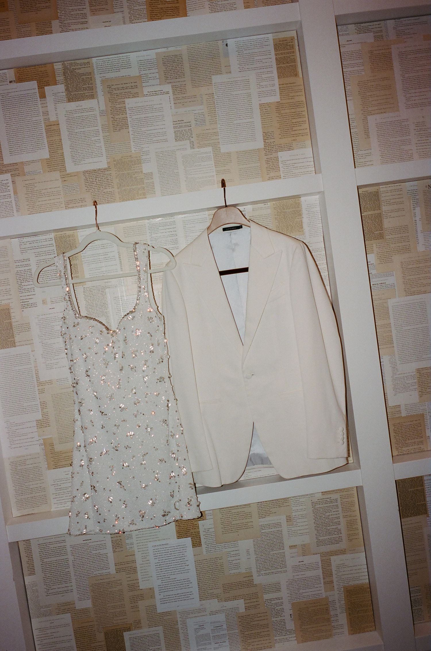 White wedding dresses and gowns hanging on display against a beige wall covered in paper.