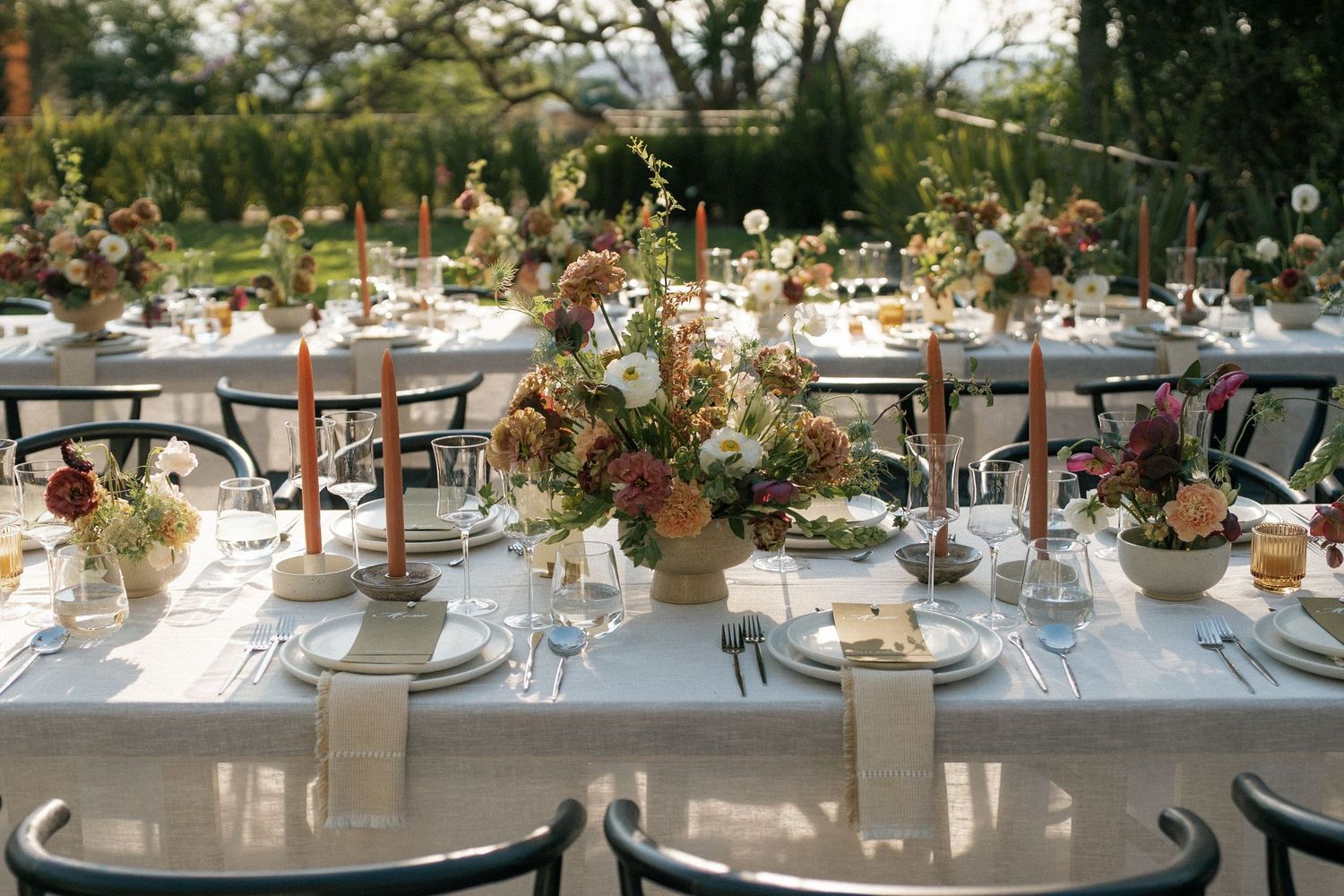Romantic outdoor wedding table setting with delicate floral centerpieces.
