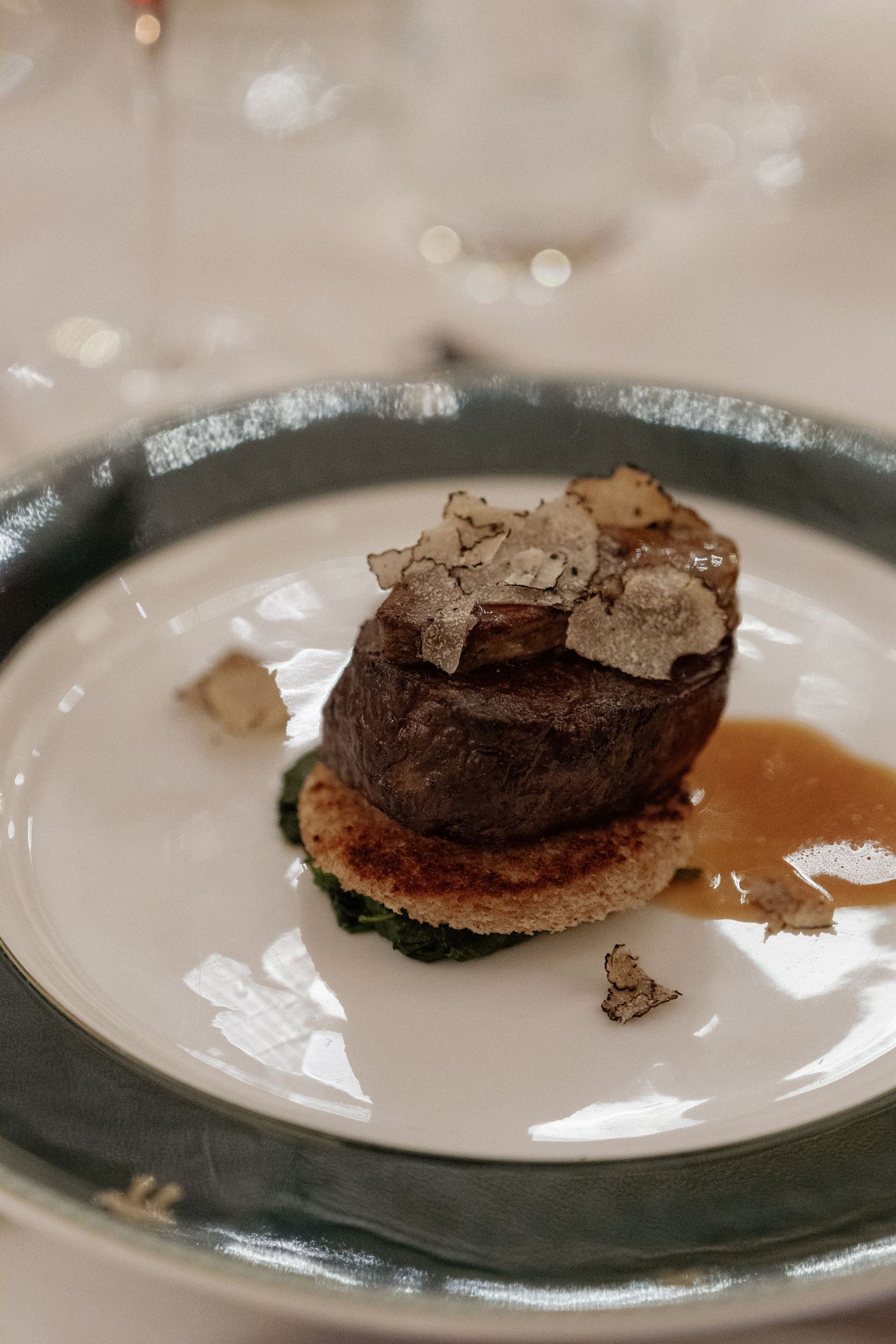 Elegant filet mignon topped with shaved white truffle on silver-rimmed plate at fine dining event.