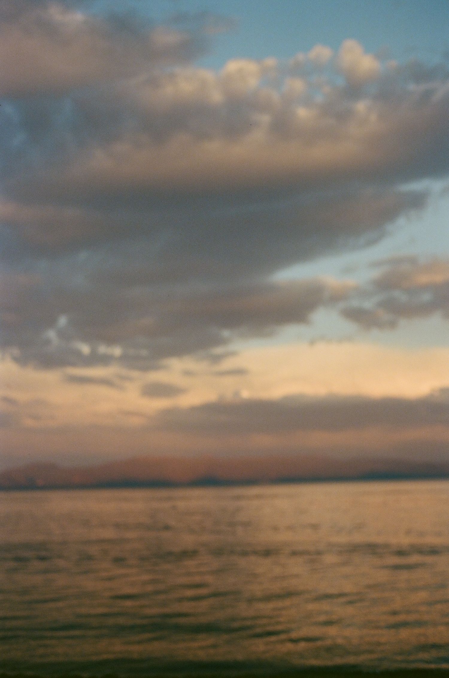 Sunset over calm ocean waters with dramatic cloudy sky.