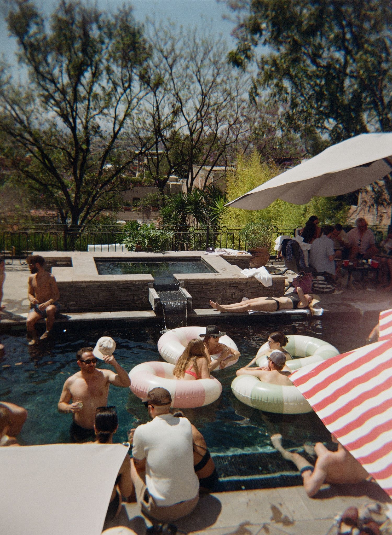 People relaxing in a pool with inflatable tubes and striped floats during a sunny summer day. San Miguel, Mexico wedding