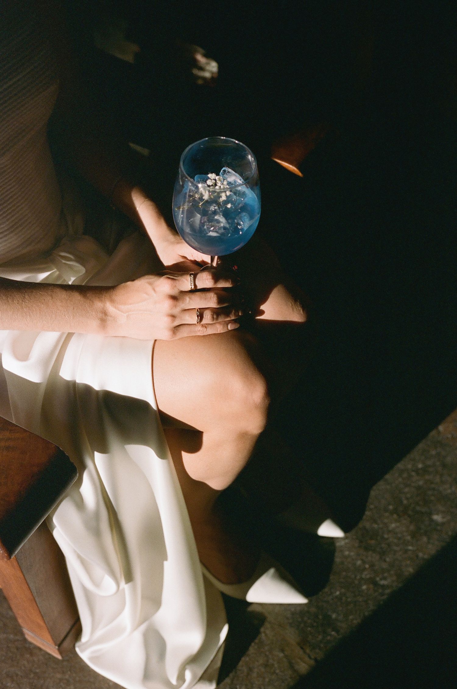 Hands holding blue glassware in dramatic lighting at an event.