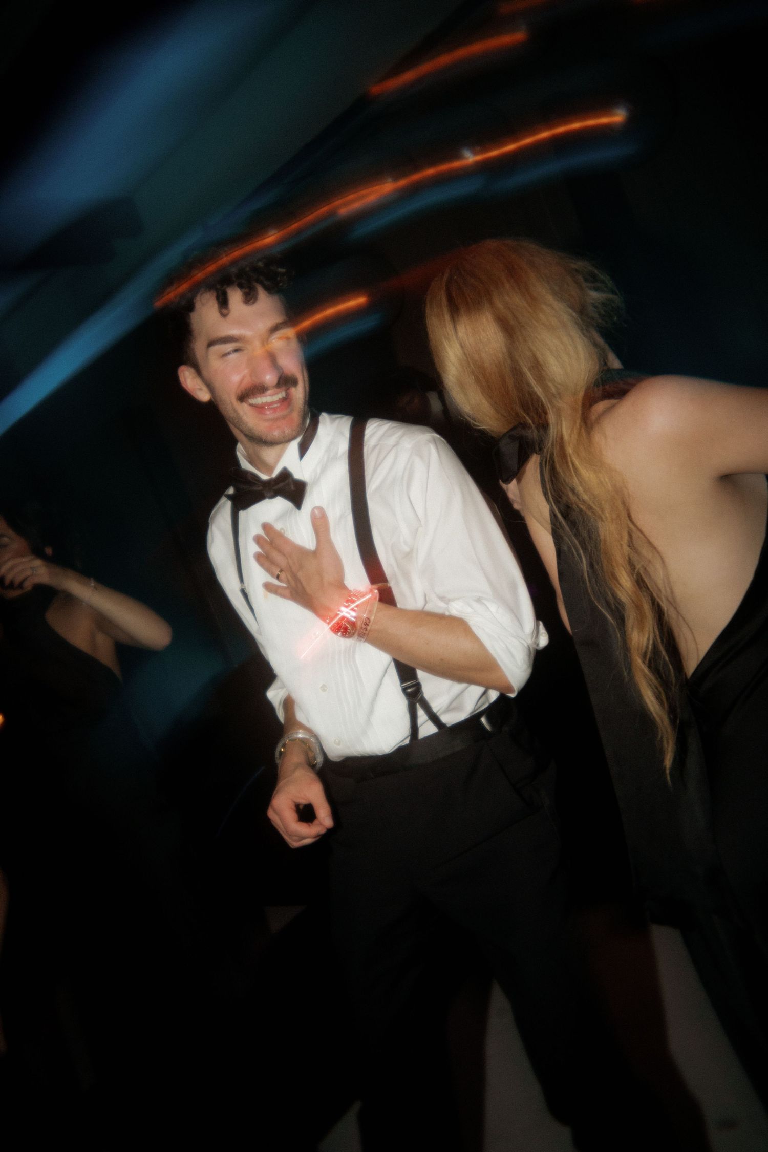 Party guests dancing and laughing under colorful lighting effects.