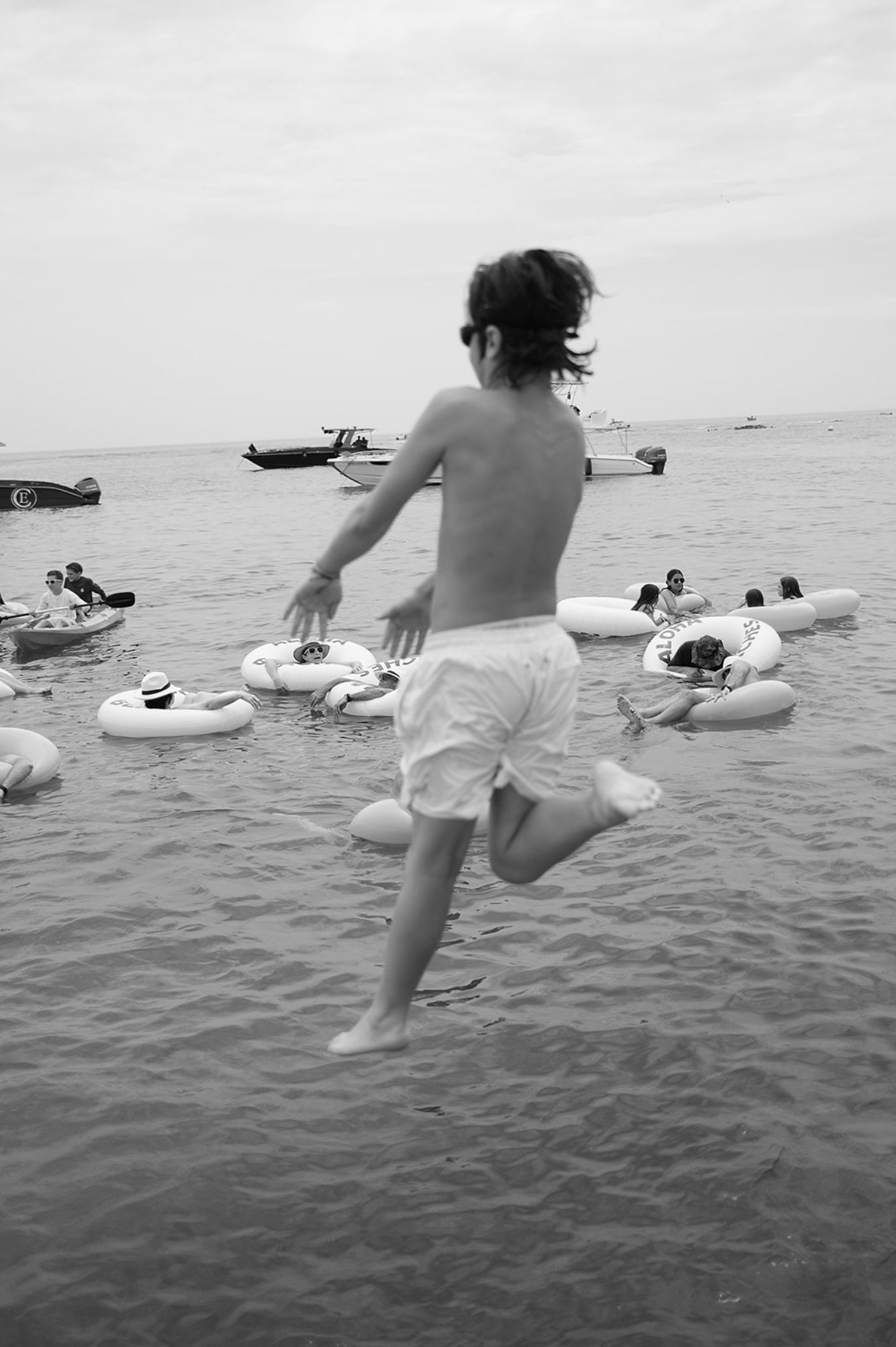Black and white sequence of someone jumping into the ocean from a boat with floating tubes nearby.