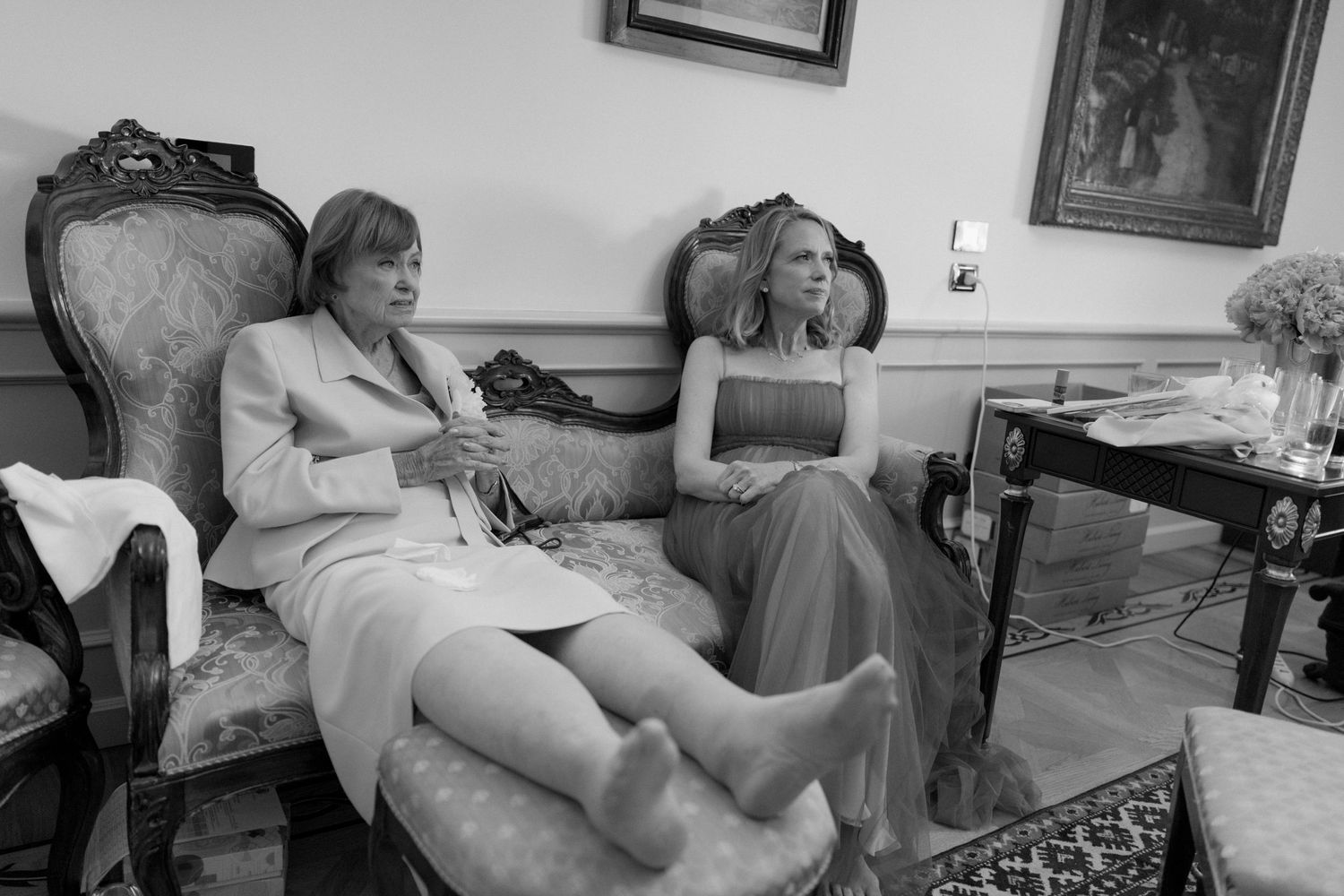Two women sitting in elegant chairs in a classic interior, captured in black and white photography.