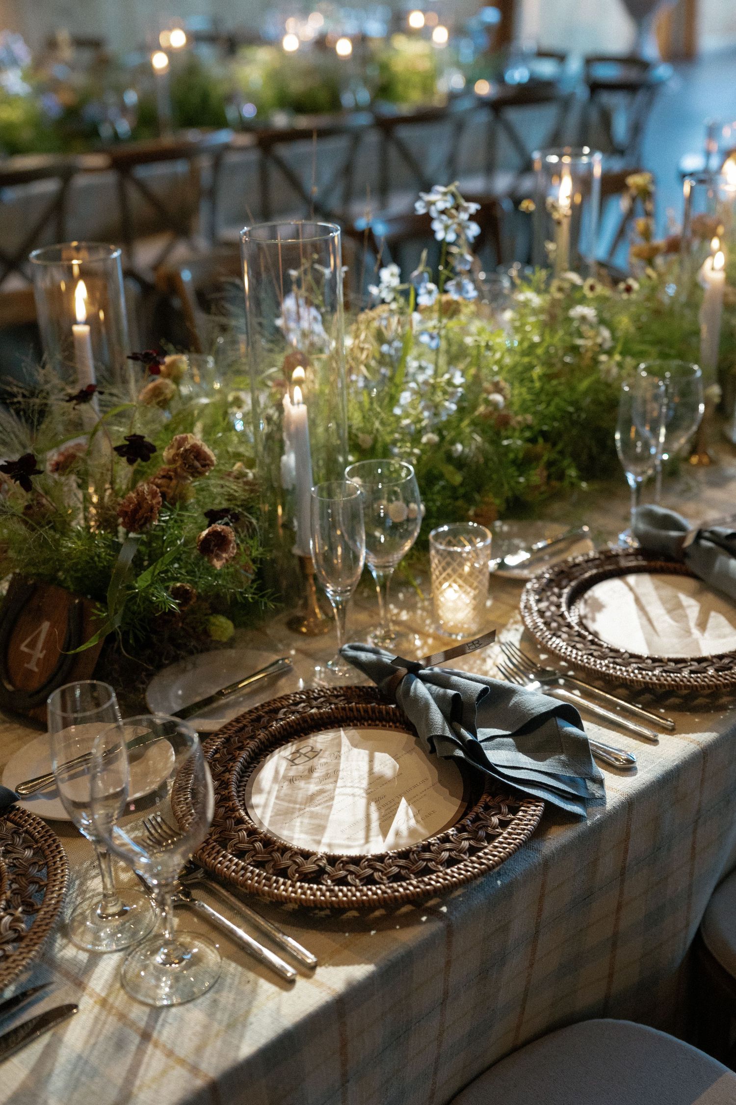 Elegant table setting with crystal glasses, ornate chargers, and greenery centerpieces.