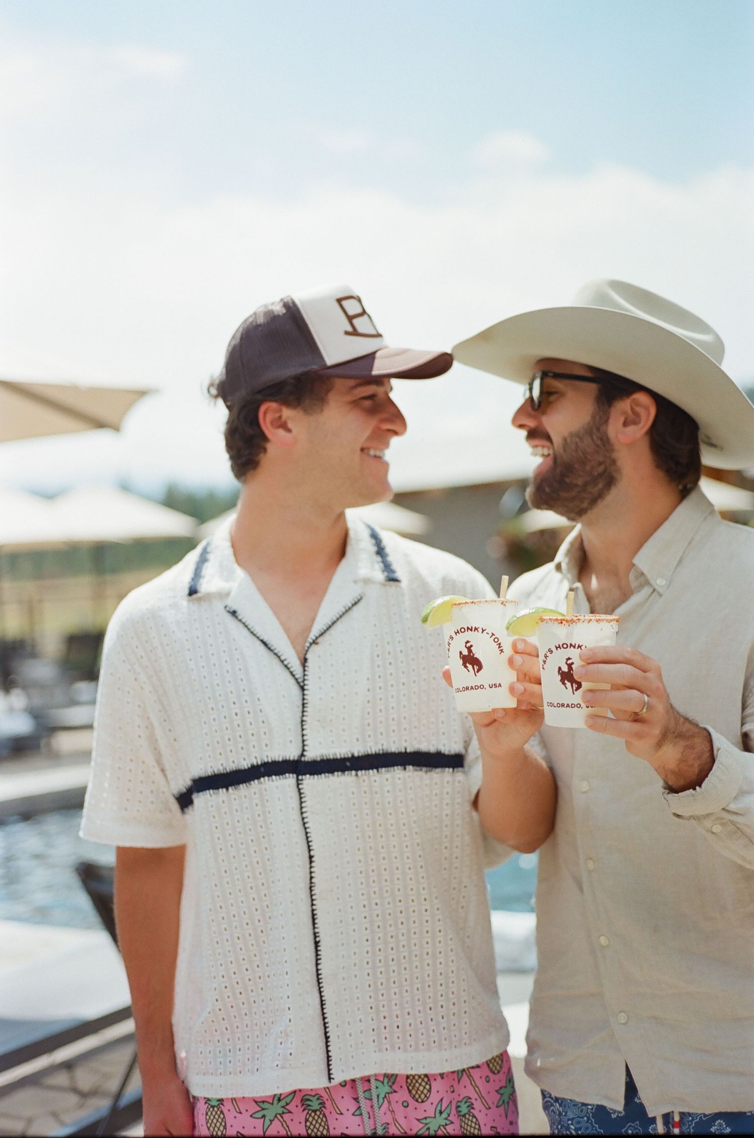 Two people in white polo shirts sharing drinks and laughing together outdoors.