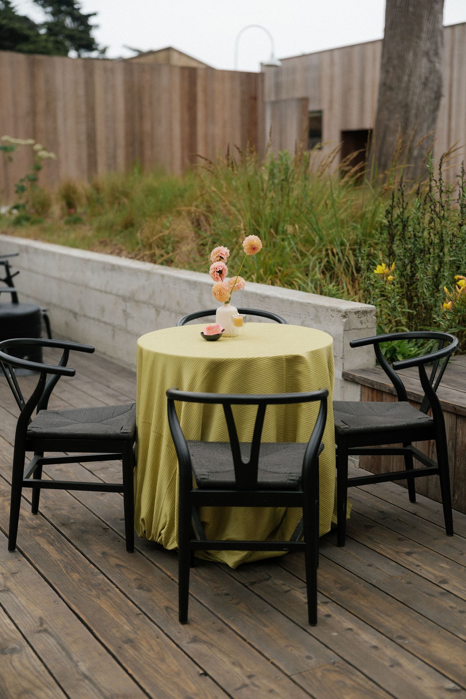 Outdoor seating area with black chairs and yellow tablecloths on wooden deck.