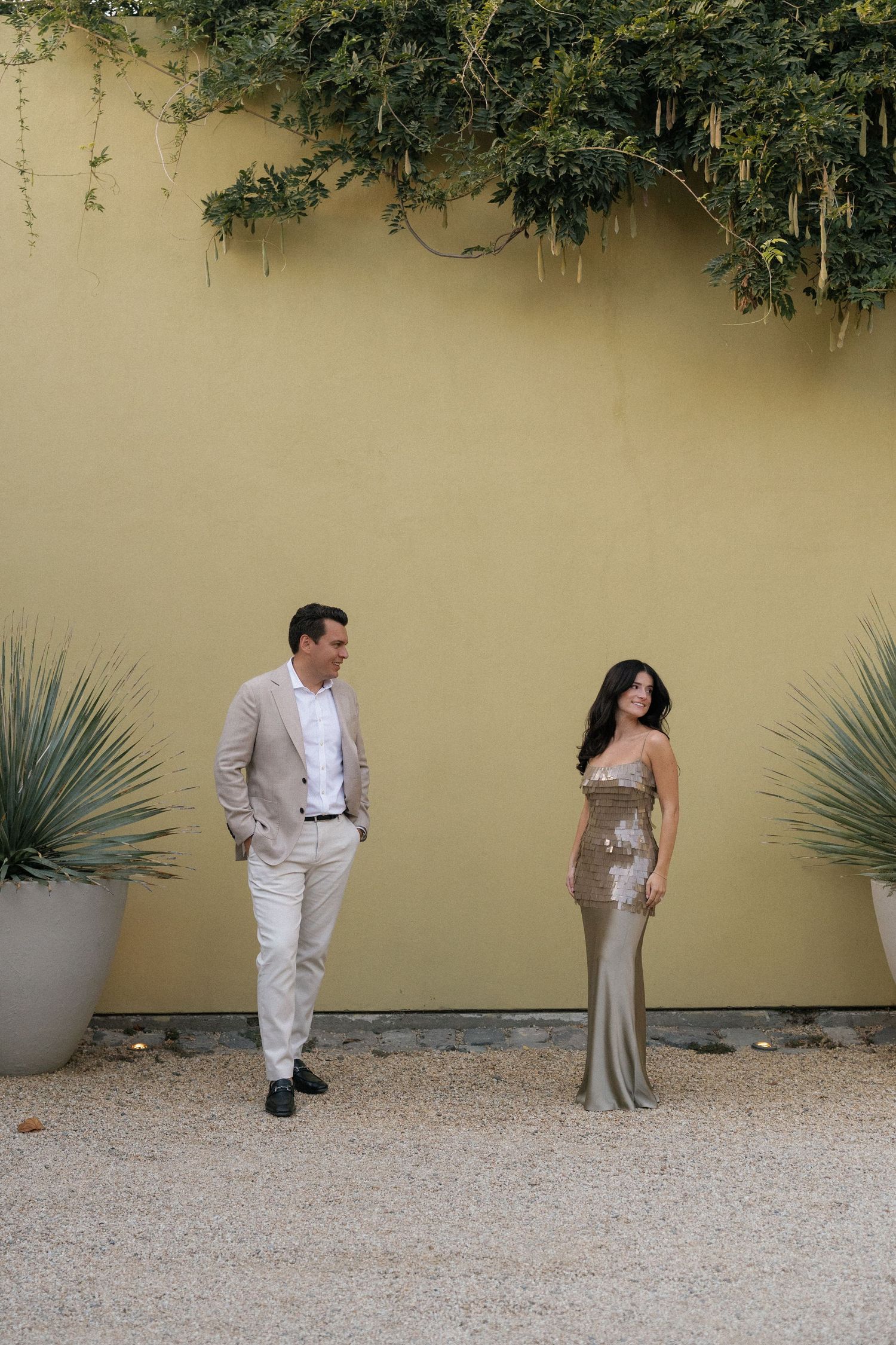 Stylish couple poses playfully against a yellow wall with desert plants.