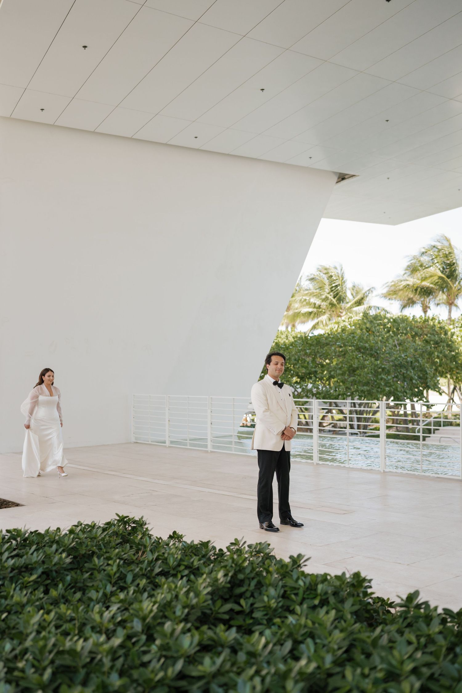 Modern white outdoor terrace space with lush greenery and palm trees in the background.