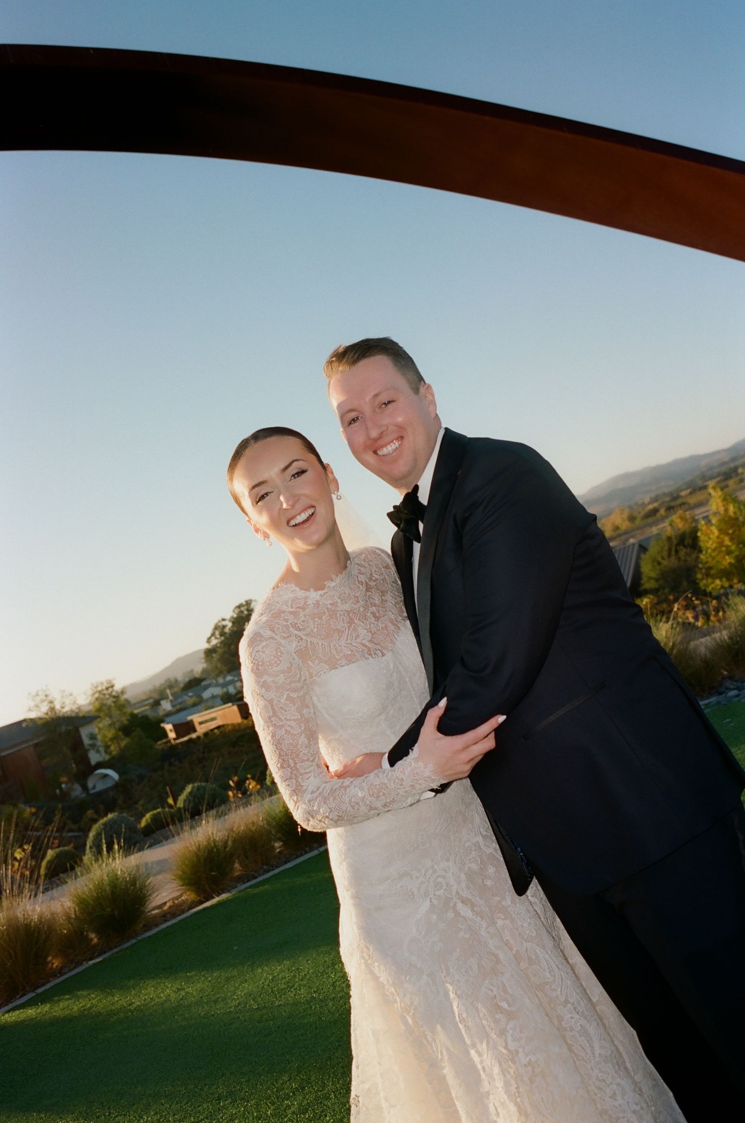 A couple in wedding attire sharing a joyful moment outdoors during sunset.