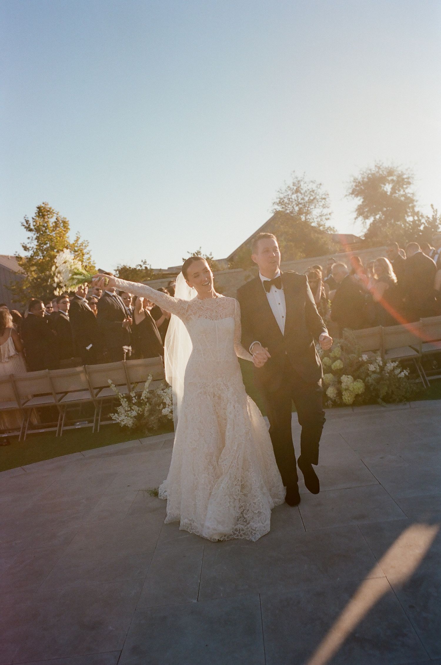 Wedding party gathered outdoors during golden hour with sunlight creating a warm glow.