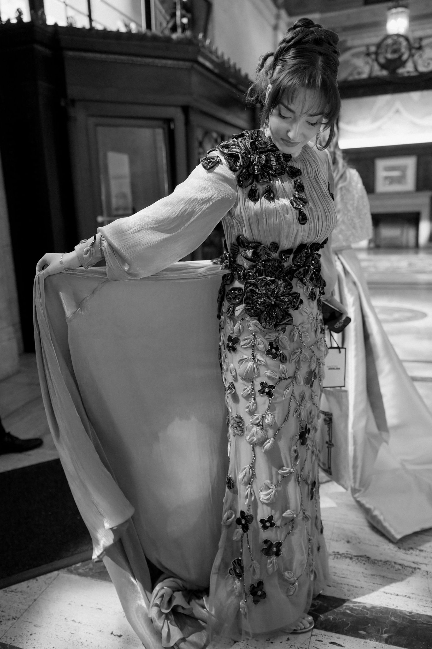 A woman in a floral dress stands in a dimly lit room.