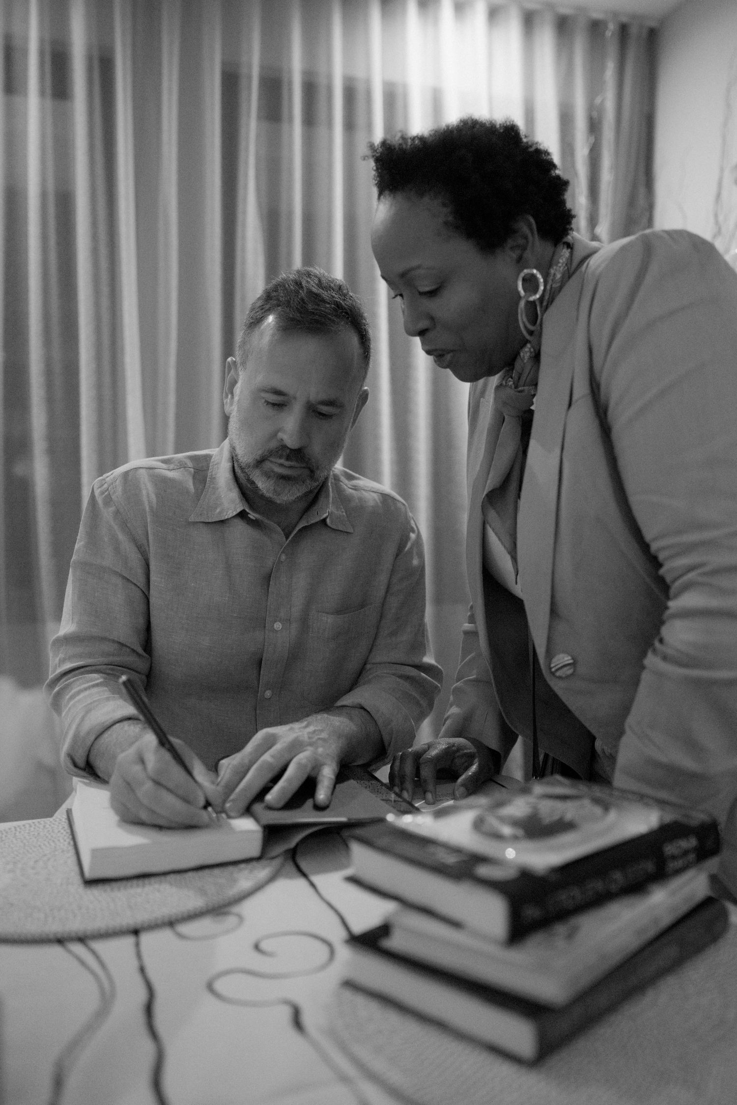 Two men, one Black and one white, are sitting at a table and looking at documents together.